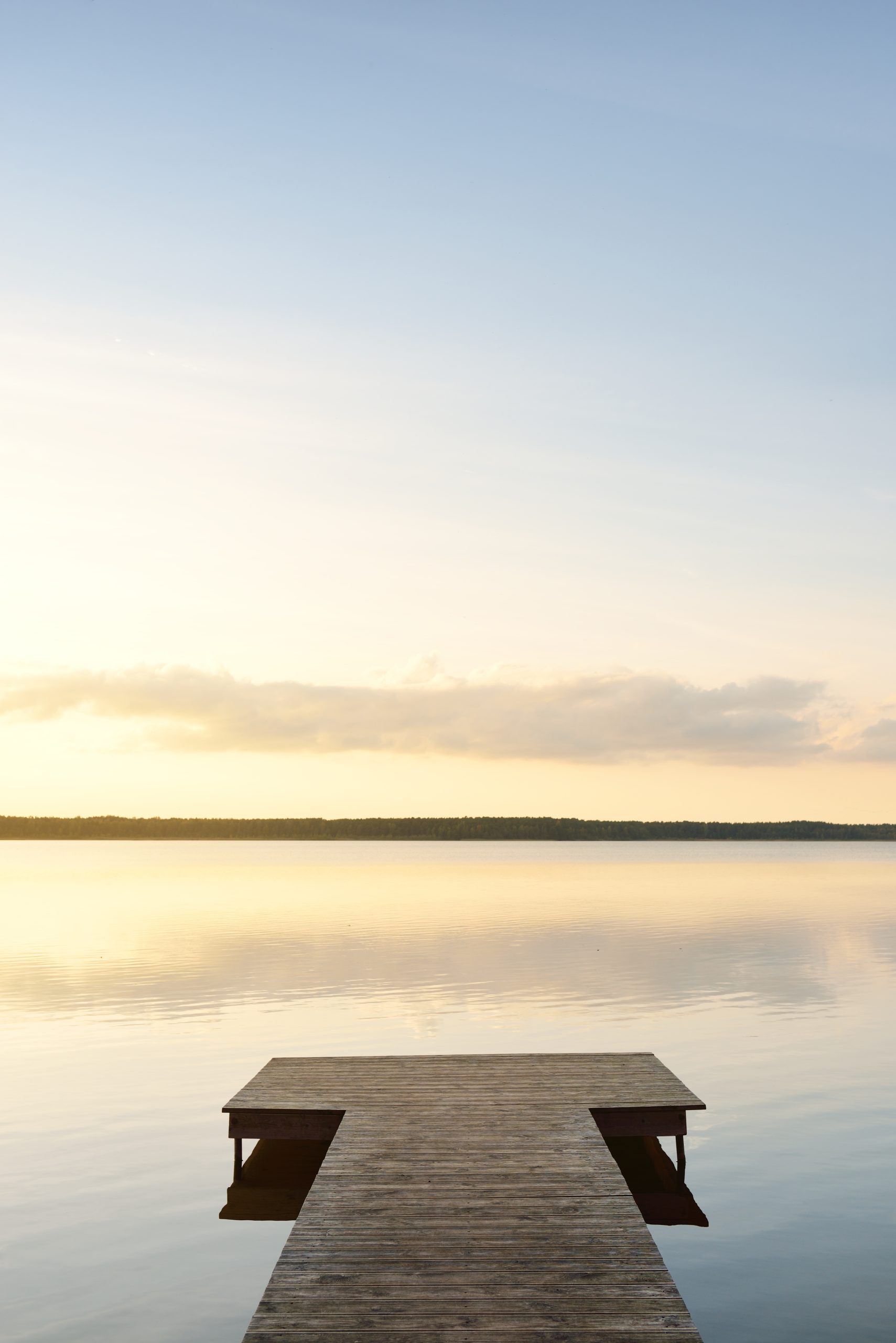 A still lake at dawn with a wooden jetty reaching into pale water