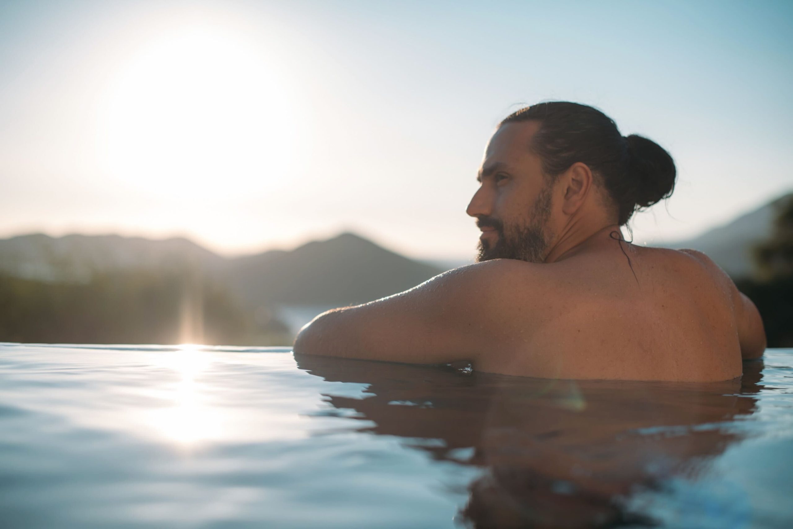 A man alone in open water at sunrise, mountains behind