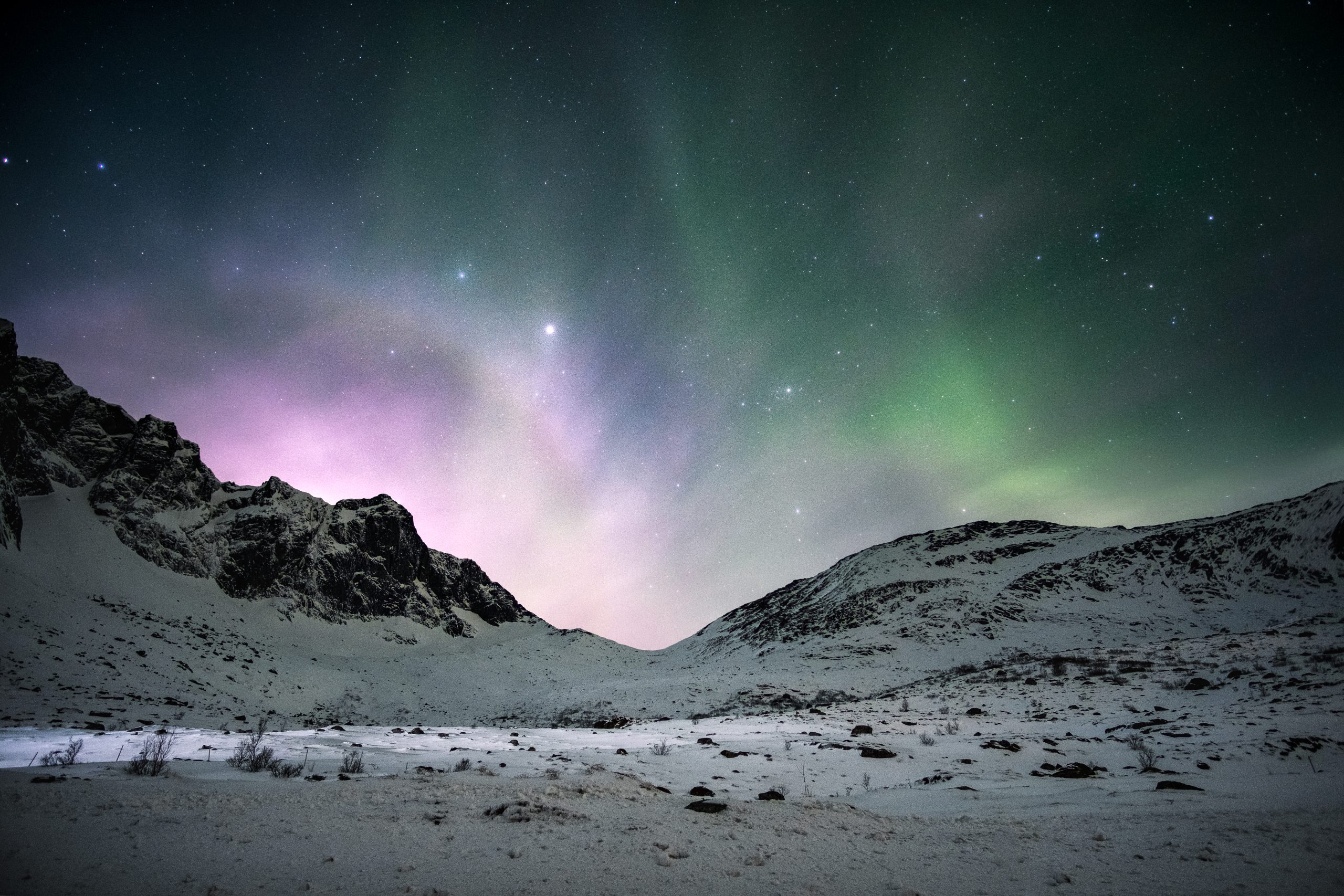 Green and violet aurora over a snow covered mountain valley