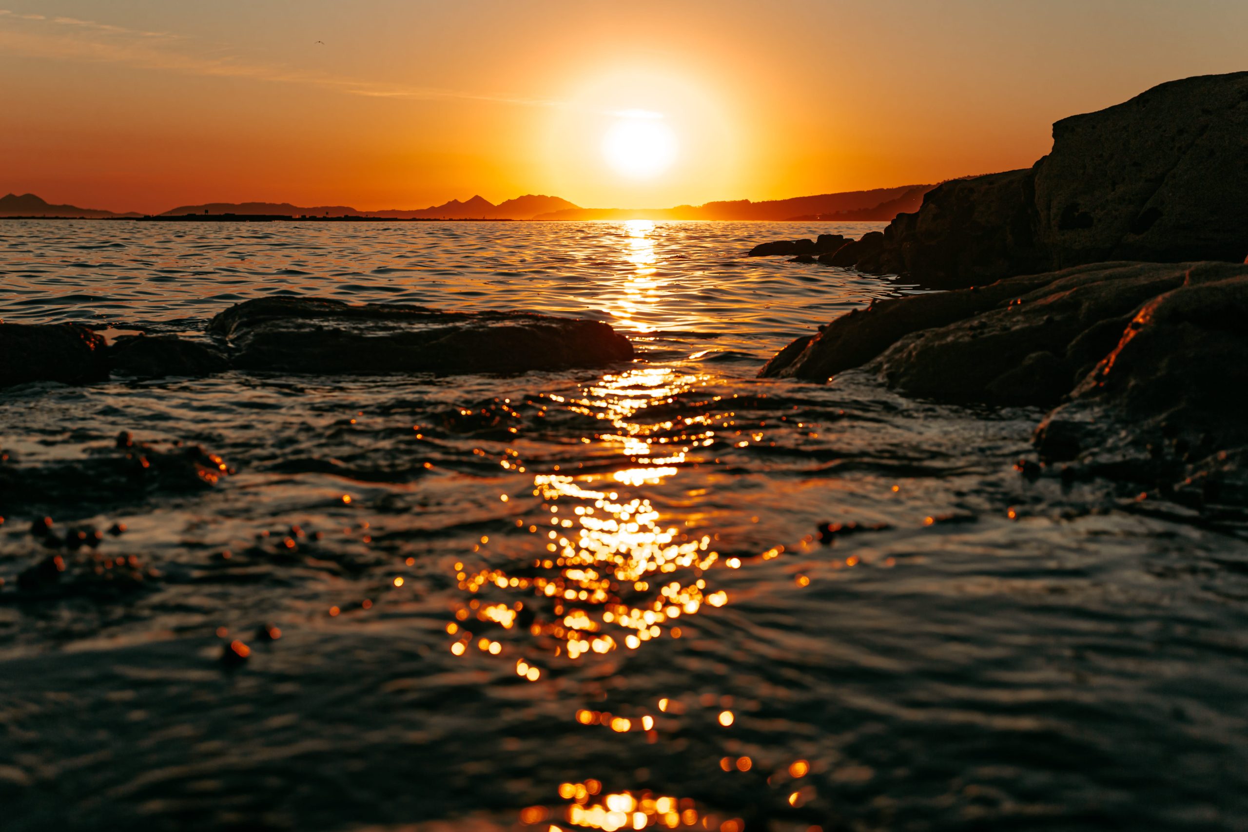 Low golden sun over the sea, light breaking across rocks and water