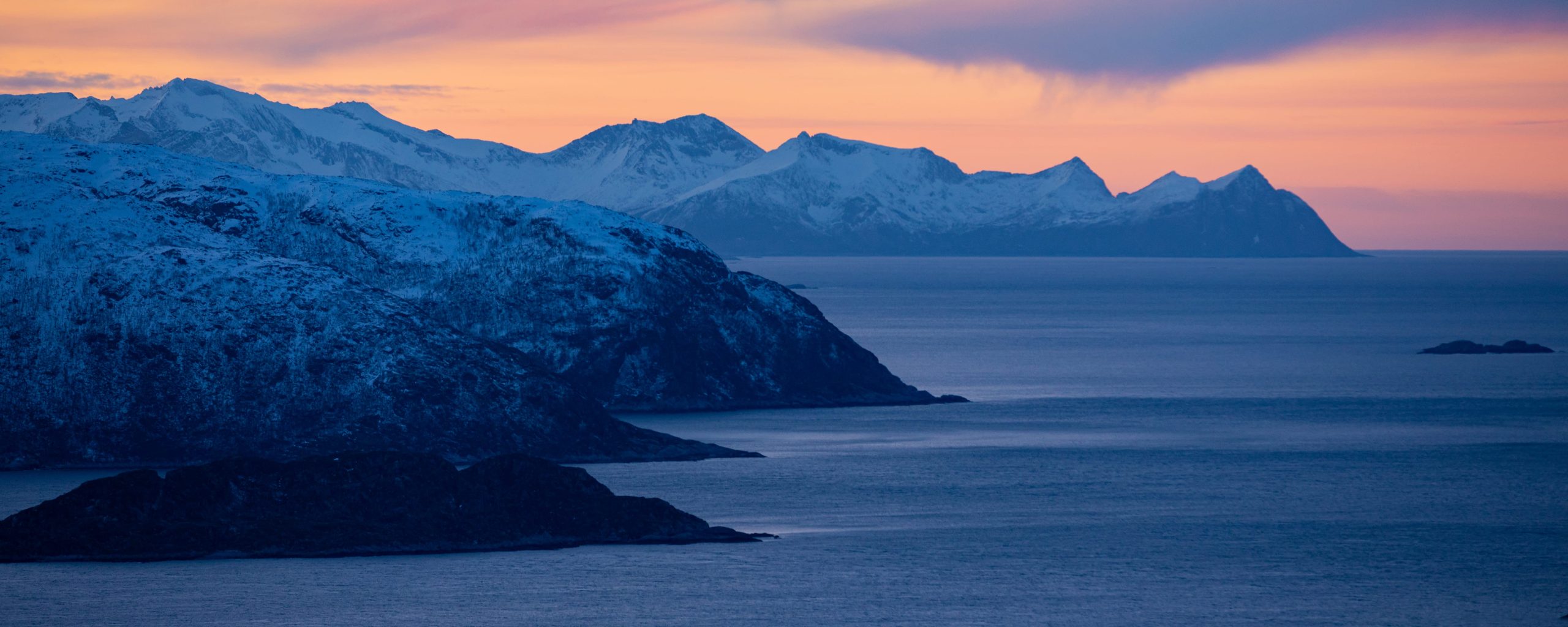 A Nordic fjord at low light, snow capped peaks above still water